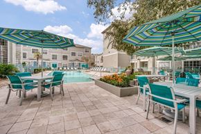 Houston apartment for rent - 2-Bedroom Luxury Apartments in Montrose, Houston, TX - The Maroneal - Pool Surrounded by the Apartment View, Featuring a Lounge Area, Patio with Stone Pavers, Tables and Mesh Chairs, and Umbrellas.