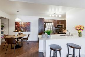 Scottsdale apartment for rent - Two-Bedroom Apartments in Scottsdale, AZ - The Sycamore at Scottsdale - Open Kitchen With White Breakfast Bar, Stainless Steel Appliances, Dark Wood Cabinets, And Adjacent Dining Area.