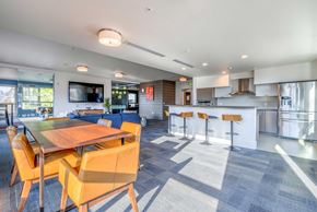 Seattle apartment for rent - South Lake Union, WA, Apartments with In-Unit Washer and Dryer - Union SLU - Clubhouse with Kitchen, Stainless Steel Appliances, Counter with Bar Seating, Dining Table and Upholstered Leather Chairs, and Lounge Area with TV.