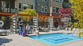 Mercer Island apartment for rent - Apartments in Mercer Island, WA with In-Unit Washer and Dryer - 77 Central - A sunlit community swimming pool and a tub area with residents relaxing on lounge chairs near a modern apartment building.