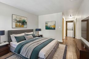 Walnut Creek apartment for rent - Apartments for Rent in Walnut Creek, CA - Park Lake at Walnut Creek - Bedroom With Tufted Headboard, Wood-Style Flooring, Bedside Lamps, Wall-Mounted Television, Dresser, and View of Laundry Closet.