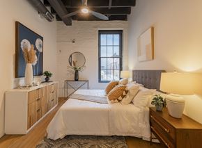St. Louis apartment for rent - A bedroom with a large bed, a wooden dresser, and a painting on the wall.