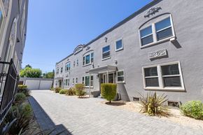 Redwood City apartment for rent - the front of a gray building with a sidewalk and a driveway