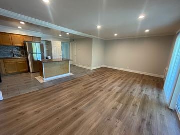 Cupertino apartment for rent - A spacious room with wooden flooring and a kitchen area with a refrigerator and cabinets.