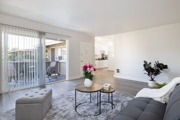 Los Gatos apartment for rent - A modern living room with a grey sofa, a round table with a vase of flowers, and a large window with blinds.