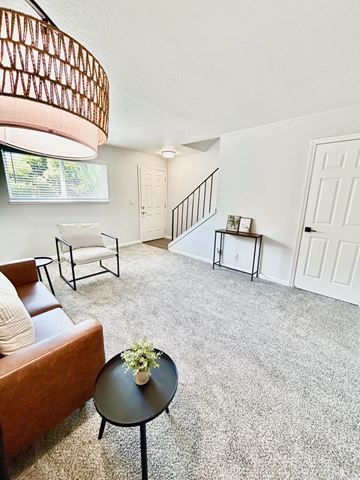 Campbell townhouse for rent - A living room with a brown couch, a small table with a plant on it, and a staircase in the background.
