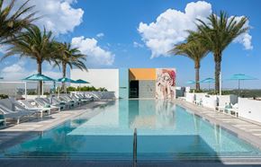 Miami apartment for rent - A large swimming pool surrounded by palm trees and lounge chairs.