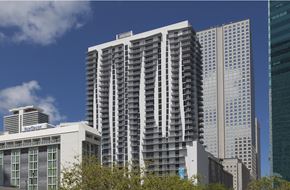 Miami apartment for rent - A tall white building with balconies is in the foreground of a cityscape.