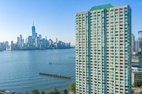 Jersey City apartment for rent - A tall building with a green roof is in the foreground with a city skyline in the background.