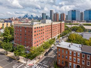 Jersey City apartment for rent - A red brick building is in the foreground of a city street.