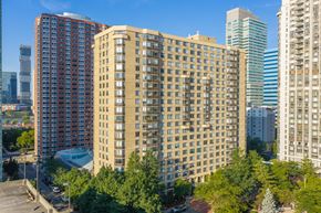 Jersey City apartment for rent - A tall building with many windows is in the foreground of a cityscape.