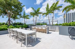 Miami apartment for rent - A white table and chairs are set up on a rooftop patio with trees in the background.