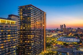 Jersey City apartment for rent - A tall building with many windows is lit up at dusk.