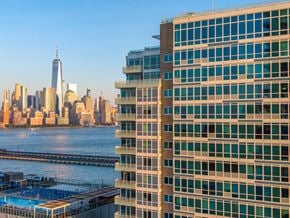 Jersey City apartment for rent - A tall building with a pool on the roof is in the foreground with a city skyline in the background.