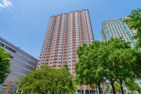 Jersey City apartment for rent - A tall red building with many windows is surrounded by trees.