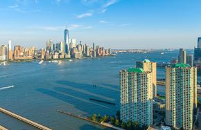 Jersey City apartment for rent - A cityscape with a body of water in the foreground and a clear blue sky above.