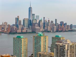 Jersey City apartment for rent - A cityscape with a body of water in the foreground and a variety of buildings, including a very tall one with a spire.