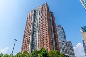 Jersey City apartment for rent - A tall red brick building stands in front of two taller buildings.