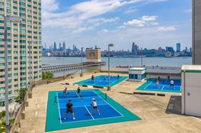 Jersey City apartment for rent - A group of people playing tennis on a court with a city skyline in the background.