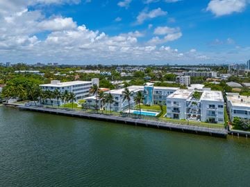 Miami apartment for rent - A large white building with a pool is situated on the edge of a body of water.