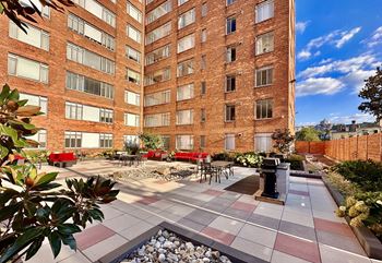 A courtyard with tables and chairs in front of a tall brick building