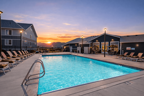 Bluffdale townhouse for rent - A sunset view of a pool area with lounge chairs and a building in the background.