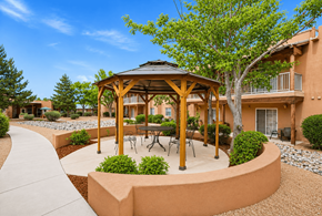 Sante Fe apartment for rent - A gazebo with a table and chairs is surrounded by bushes and trees.