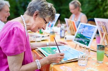 An older woman is painting a picture outdoors.