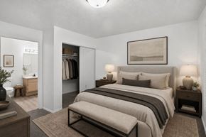 West Valley City apartment for rent - A bedroom with a large bed and a bench in front of it.