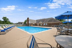 Lansing apartment for rent - A large outdoor swimming pool with a blue umbrella and chairs around it.