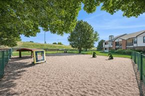 Greeley apartment for rent - A sandy playground area with a green fence and a building in the background.