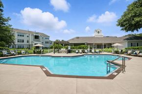 Sanford apartment for rent - A large swimming pool surrounded by a concrete patio and a white building with a tower in the background.