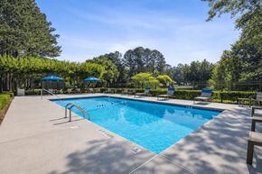 Riverdale apartment for rent - A large outdoor swimming pool surrounded by trees and lounge chairs at Emerald Pointe, Riverdale, Georgia