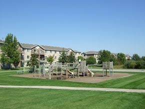 Champlin apartment for rent - A playground with swings and slides in front of apartment buildings.