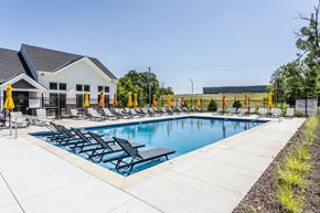 Kansas City apartment for rent - A pool with chairs and umbrellas is surrounded by a white building and a fence.