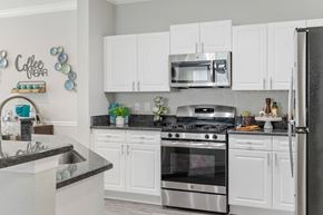 Tampa apartment for rent - A kitchen with white cabinets and a black countertop at The Grand Reserve at Tampa Palms Apartments, Tampa