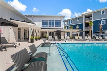 A swimming pool with lounge chairs and umbrellas in front of a building 