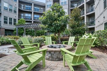 A fire pit surrounded by green chairs in a courtyard.