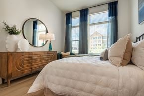 Charlotte apartment for rent - A bedroom with a large bed, a wooden dresser, and a round mirror on the wall.