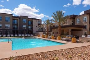 Glendale apartment for rent - A swimming pool is surrounded by chairs and palm trees in front of a building.