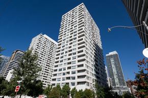 Toronto apartment for rent - A tall white building stands in front of other buildings on a sunny day.