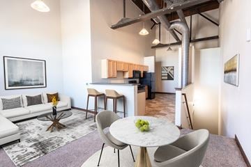 Sioux Falls apartment for rent - A modern living room with a white couch, a round table with a bowl of fruit on it, and a kitchen area in the background.