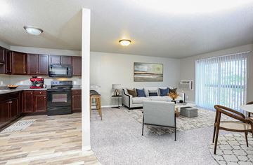 Sioux Falls apartment for rent - A living room with a grey couch and a kitchen area with brown cabinets.