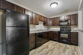 Sioux Falls apartment for rent - A black refrigerator in a kitchen with wooden floors and brown cabinets.