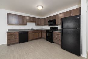 Sioux Falls apartment for rent - A black refrigerator is in a kitchen with brown cabinets.