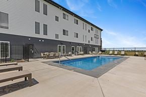 Rapid City apartment for rent - A large outdoor swimming pool is surrounded by a concrete patio and wooden benches.