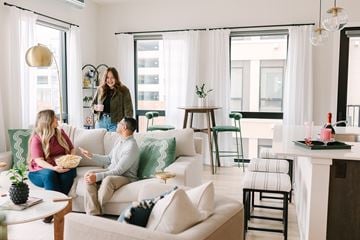 Des Moines apartment for rent - A woman is standing in a living room with a man sitting on a couch and a woman sitting on a chair.