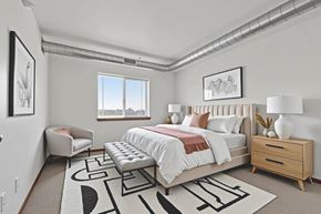 Sioux Falls apartment for rent - A bedroom with a large bed, a bench, and a rug with a black and white design.