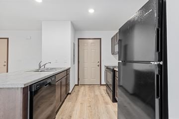 Rapid City townhouse for rent - A black refrigerator is in the foreground of a kitchen with wooden floors and white walls.