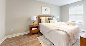 Maple Shade apartment for rent - A bedroom with a large bed and a nightstand with a lamp.